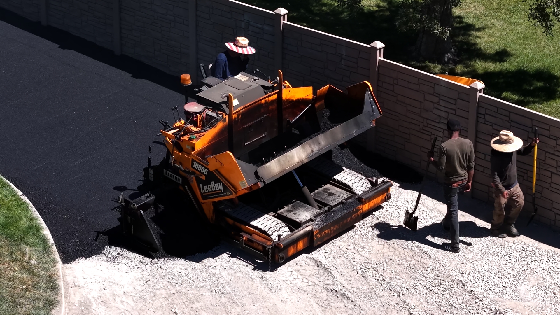 Top-down aerial view of J&C Asphalt paver and crew laying asphalt on a large commercial lot